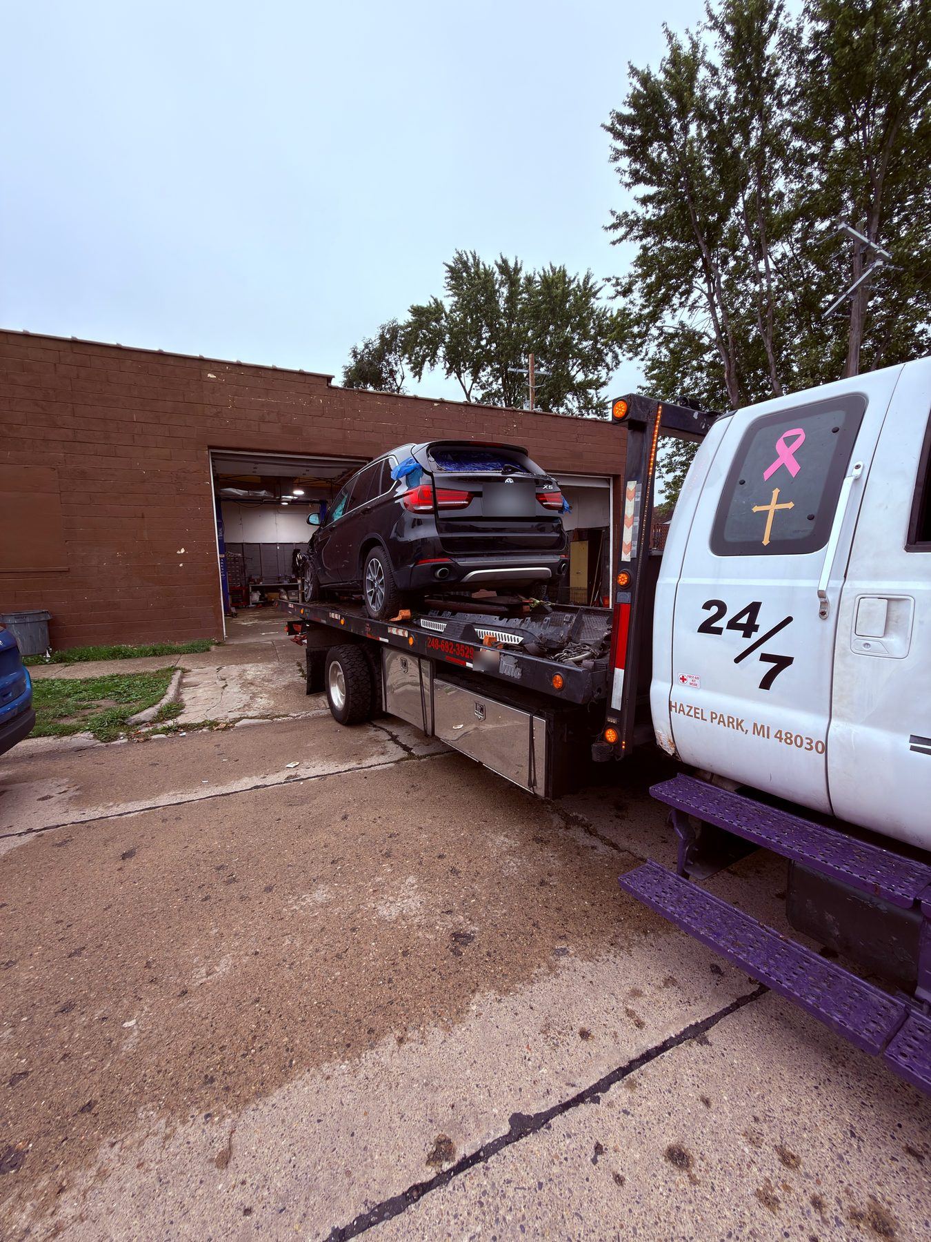 Black BMW SUV loaded on the James Towing flatbed outside a Hazel Park garage