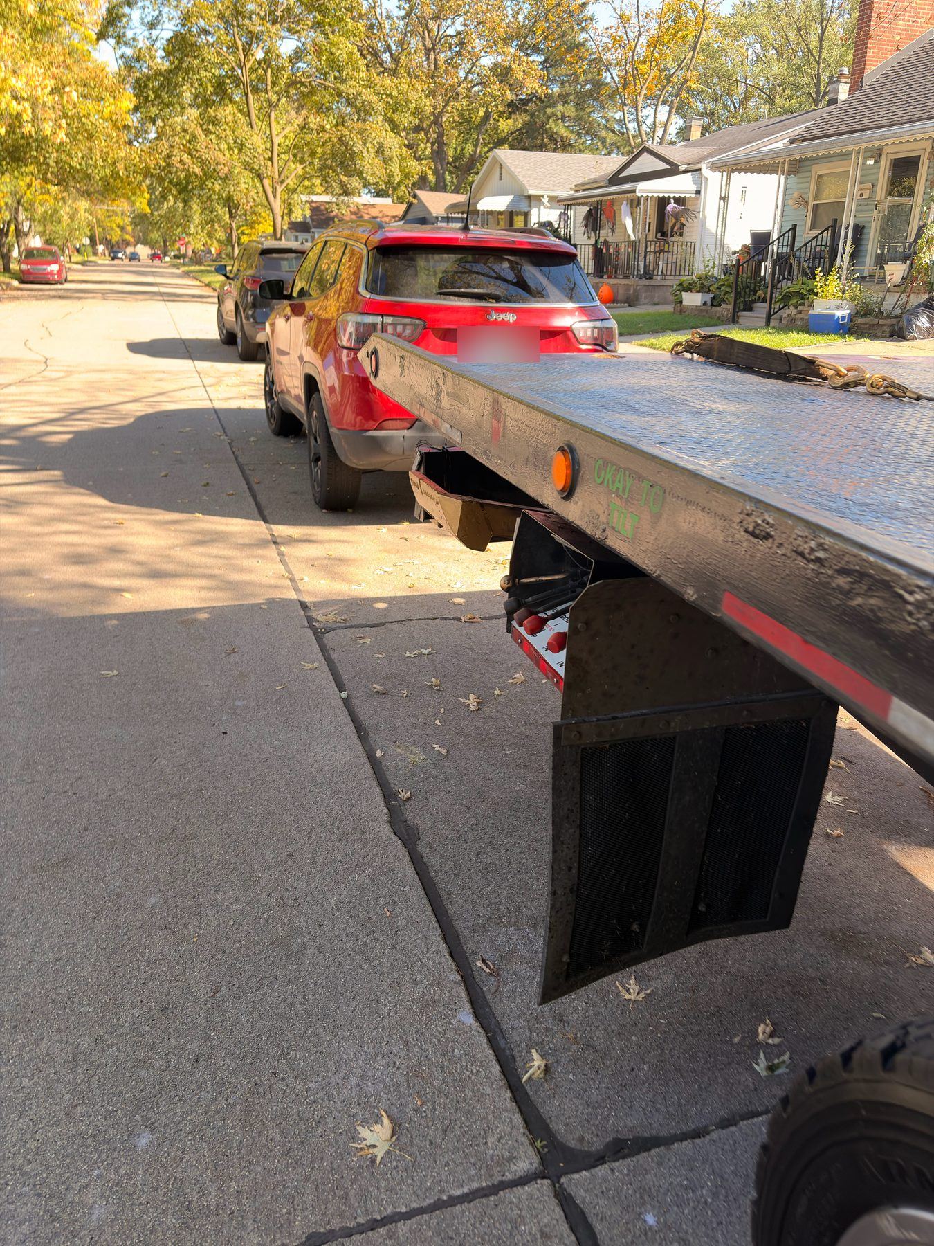 James Towing flatbed bed tilted at the curb behind a red Jeep on a Metro Detroit street